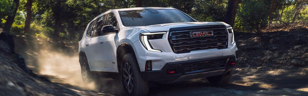 White GMC SUV driving off-road through a forest trail kicking up dust.
